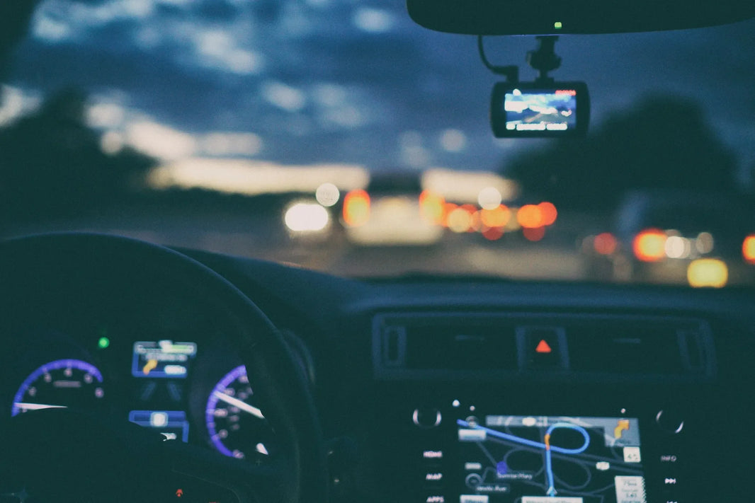 The driver’s seat of a car seen from over the driver’s shoulder, with a GPS tracker on the windscreen.