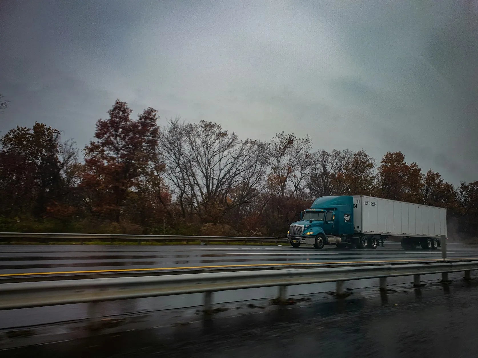 A green truck pulling a white trailer driving on a tree-and-fence-lined road, with blurring to indicate motion, connecting to the question, “What is the best GPS for truck drivers?”
