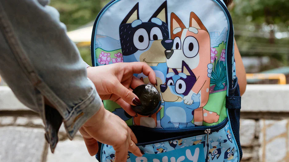 Parent placing a small GPS tracker for kids into a child's backpack front pocket