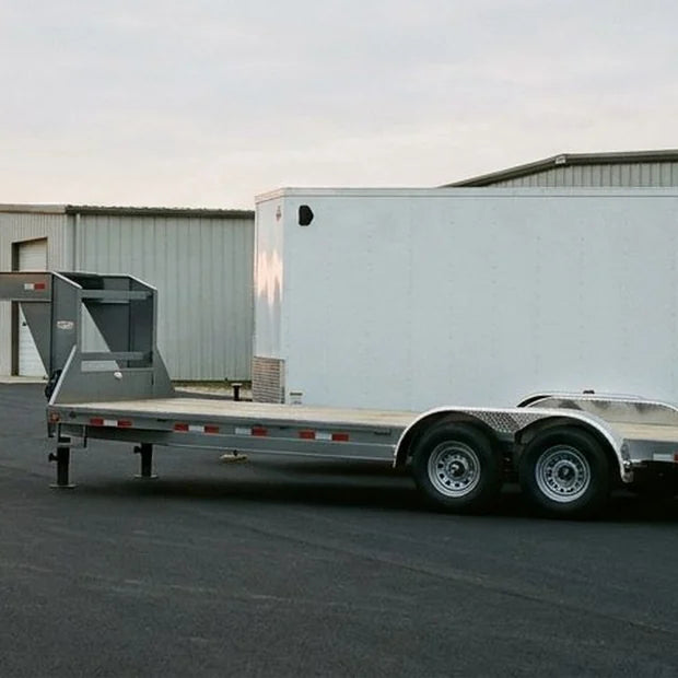 A gooseneck deck-over trailer parked on the apron of a fabrication shop at dusk